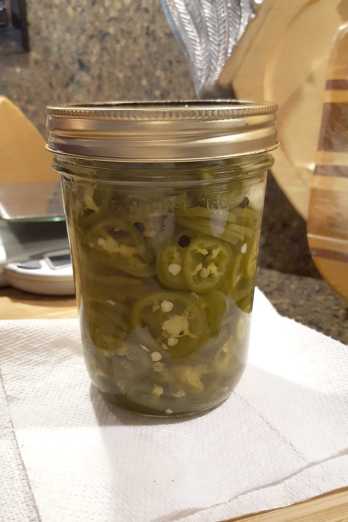 Jar filled with jalapeno slices and brine, closed with canning lid and ring.