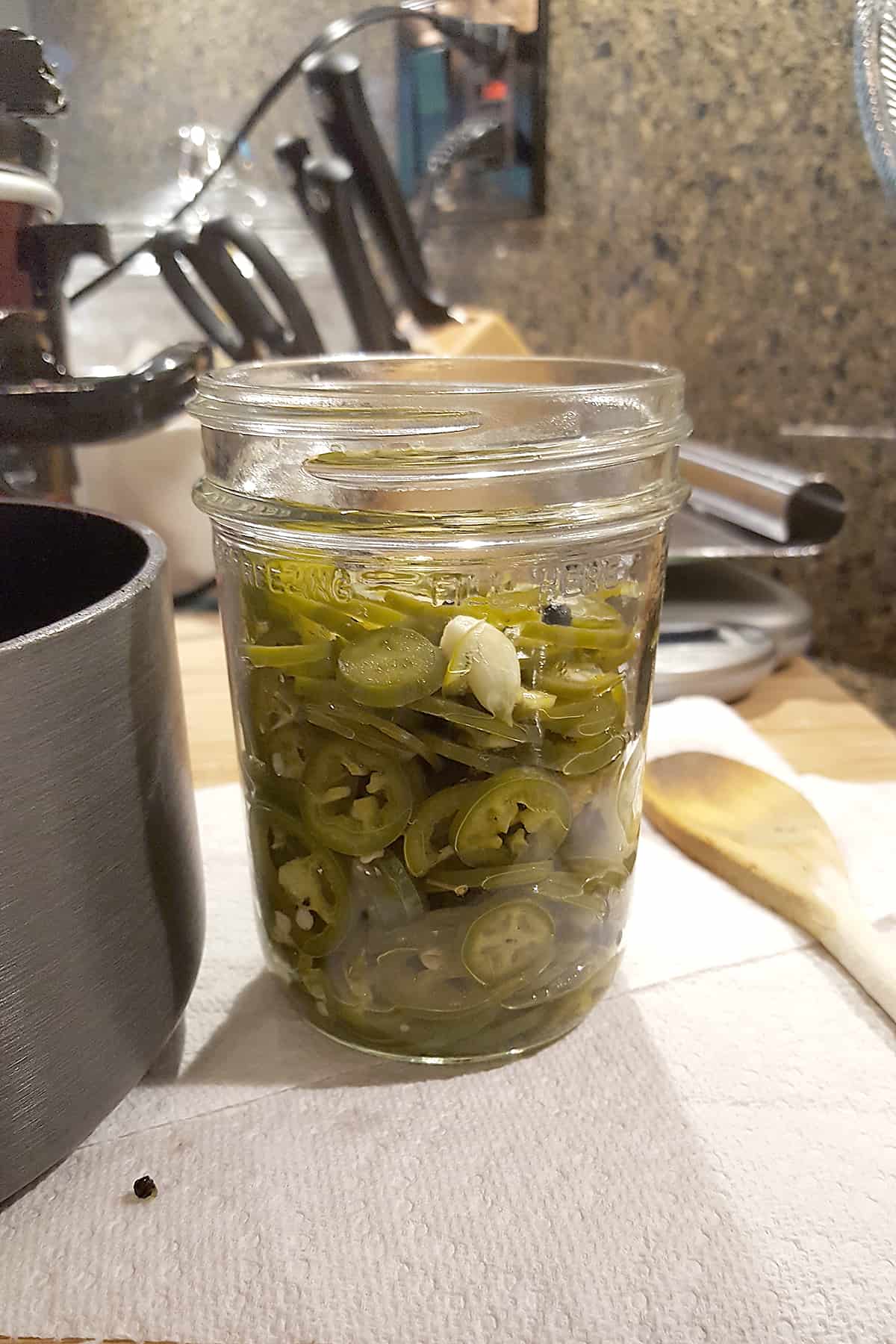 Canning jar containing cooked jalapeno slices and garlic cloves.
