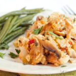 A serving of chicken and rice casserole with mushrooms and herbs on a plate, accompanied by cooked green beans.