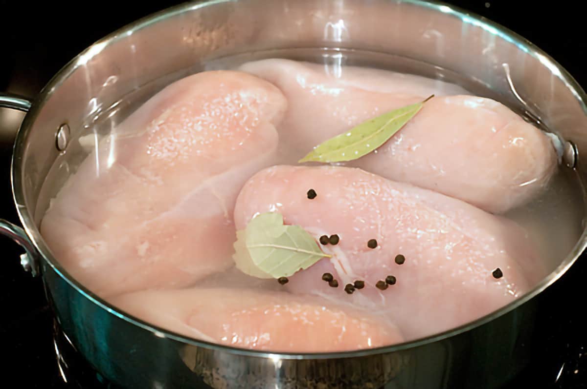 Chicken breasts poaching with bay leaves and peppercorns