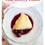 A slice of lemon pudding cake with cherry coulis and cherries on a white plate, with a spoon on the side.