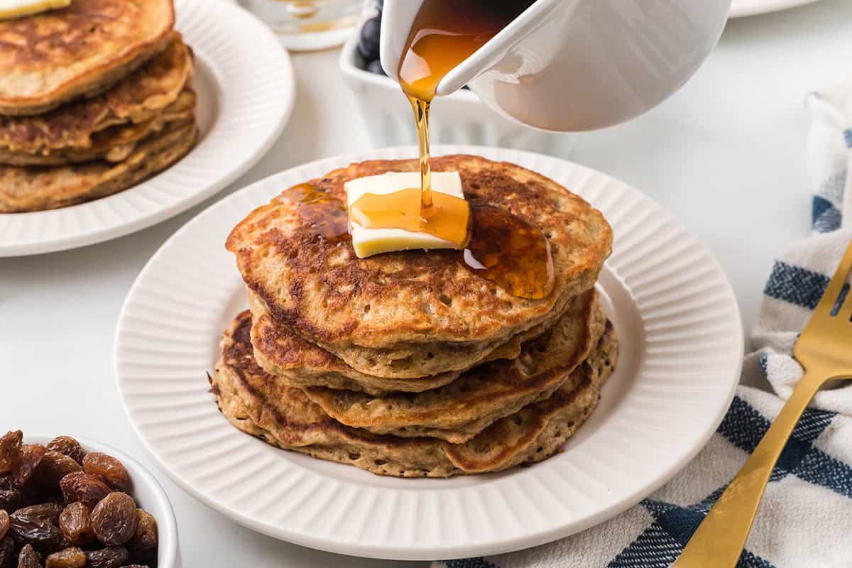 Syrup being poured over a stack of pancakes.
