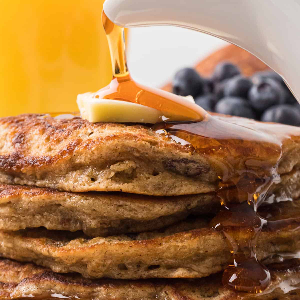 Syrup being poured over a stack of pancakes.