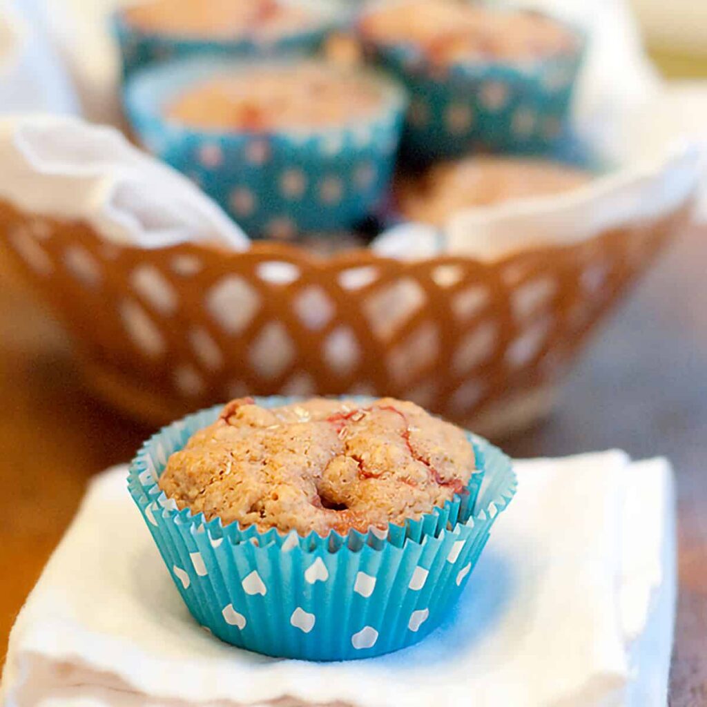 A strawberry lemon muffin sitting on a napkin with a basket of muffins in the background.