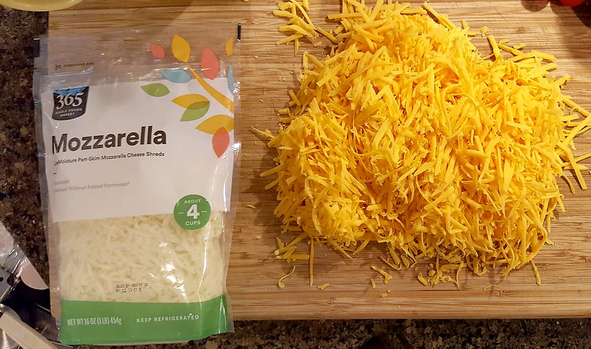 A bag of pre-shredded mozzarella cheese and one pound of hand grated Cheddar cheese on a board.