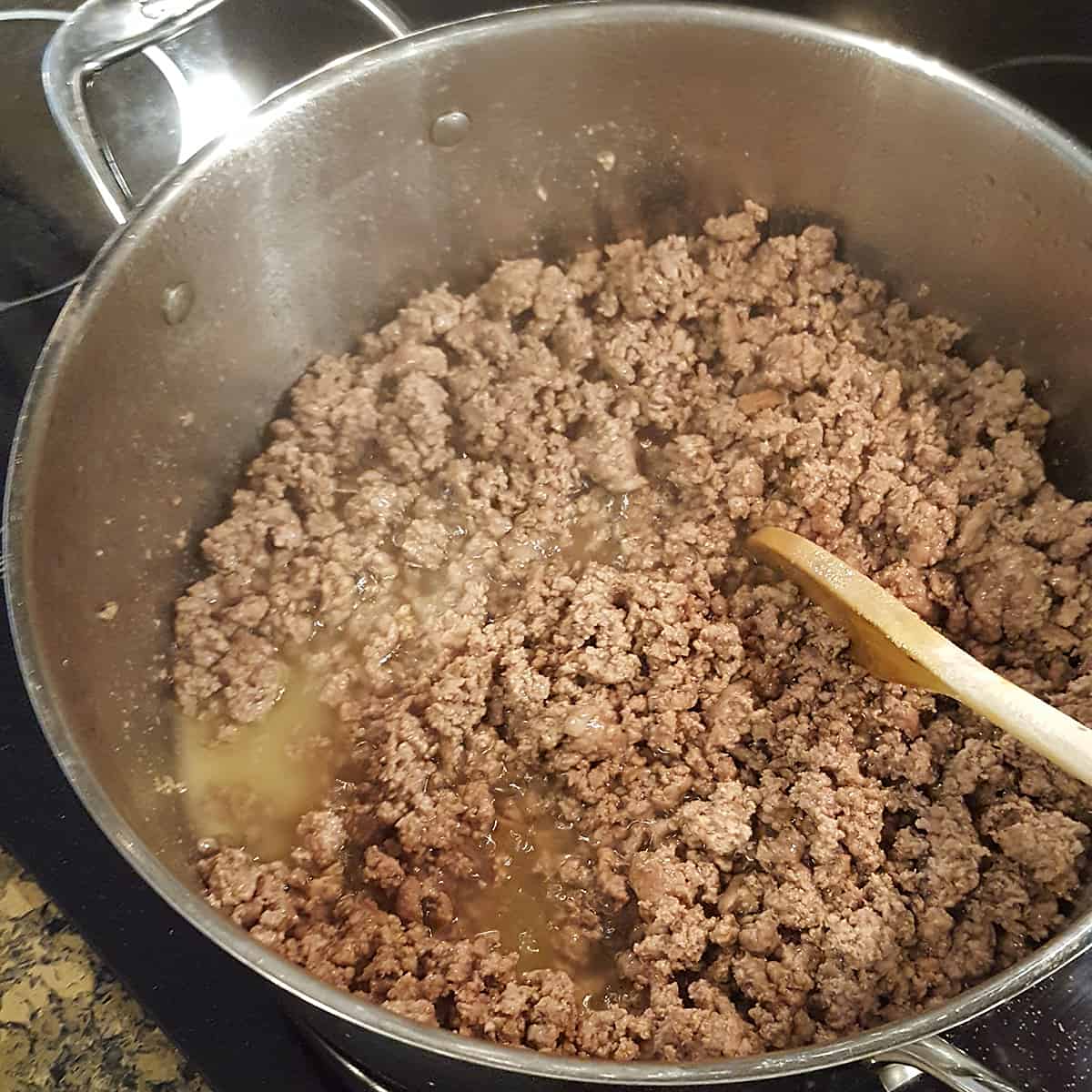 Pan with browned ground beef and a wooden spoon.