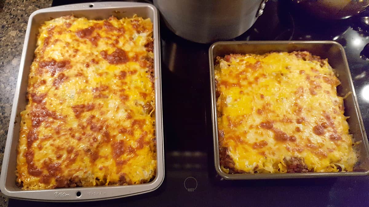 The two pans of lasagna after baking sitting on the stovetop to cool before serving.