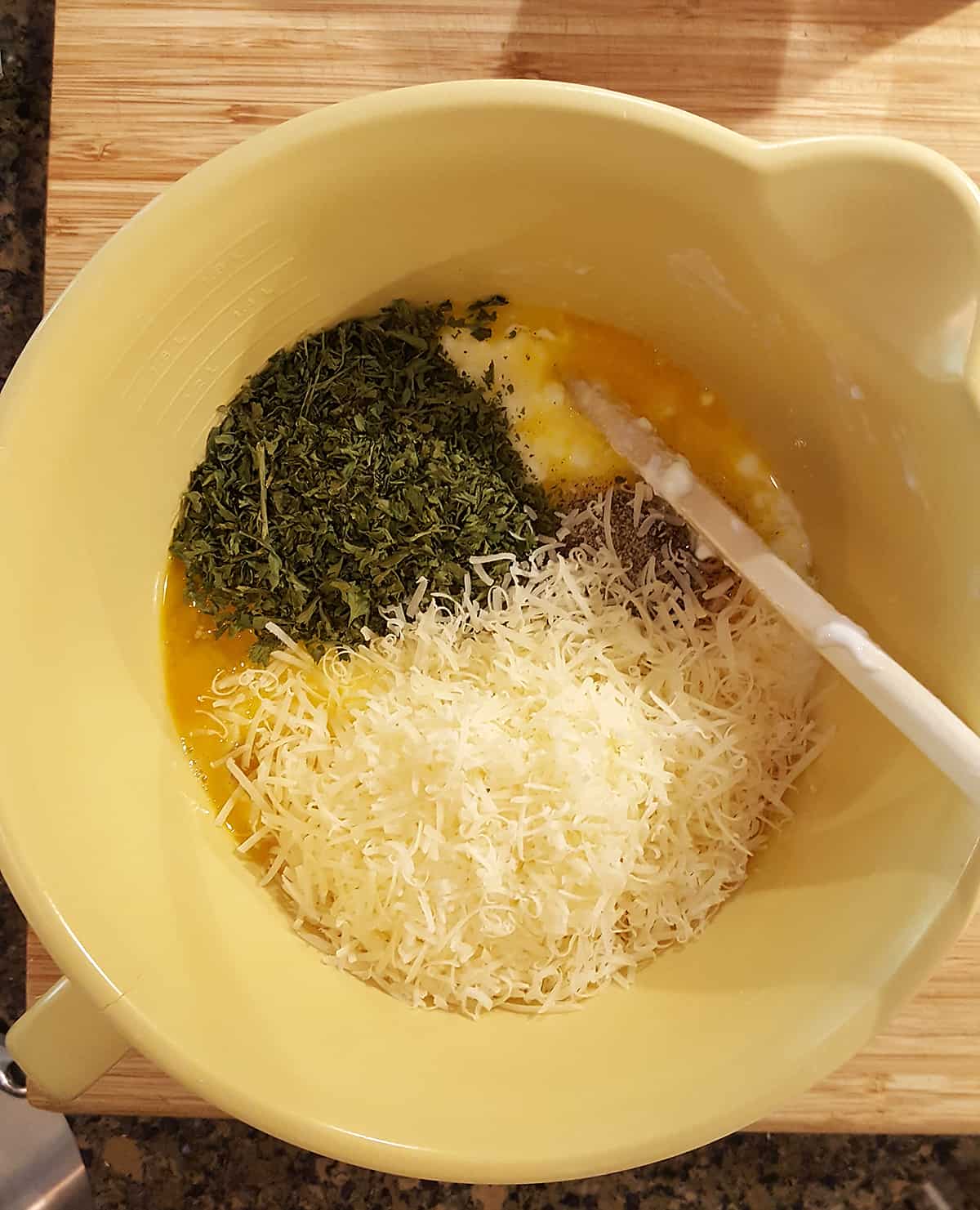Mixing bowl holding the filling ingredients of cottage cheese, eggs, parsley, and Parmesan cheese.