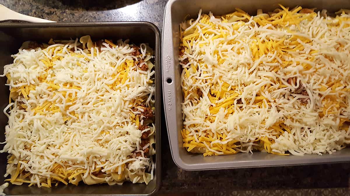 Two pans (one 9x9 and one 9x13) filled with the assembled egg noodle lasagna.