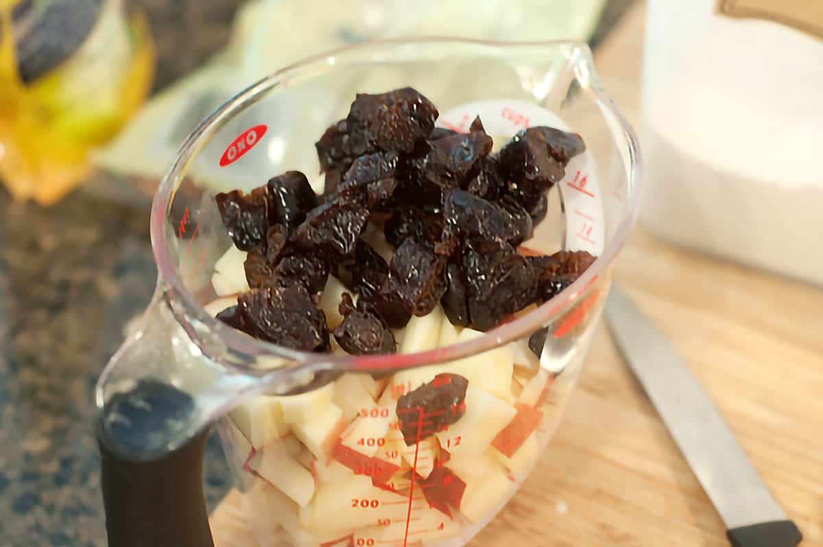 Chopped apples and prunes in a measuring cup.