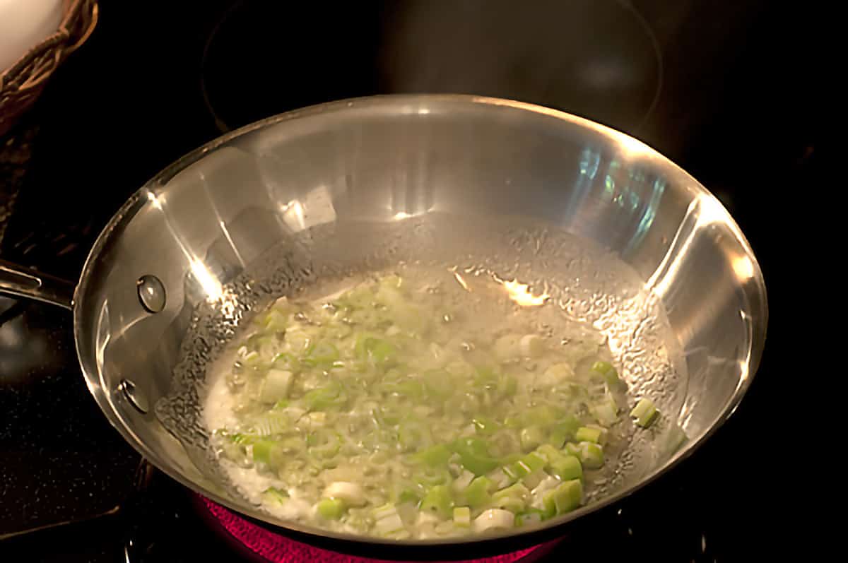 Green onions cooking in butter in a skillet.