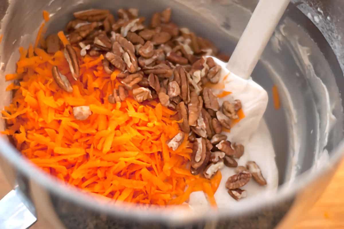 Shredded carrots and nuts being folded into the batter in mixing bowl.