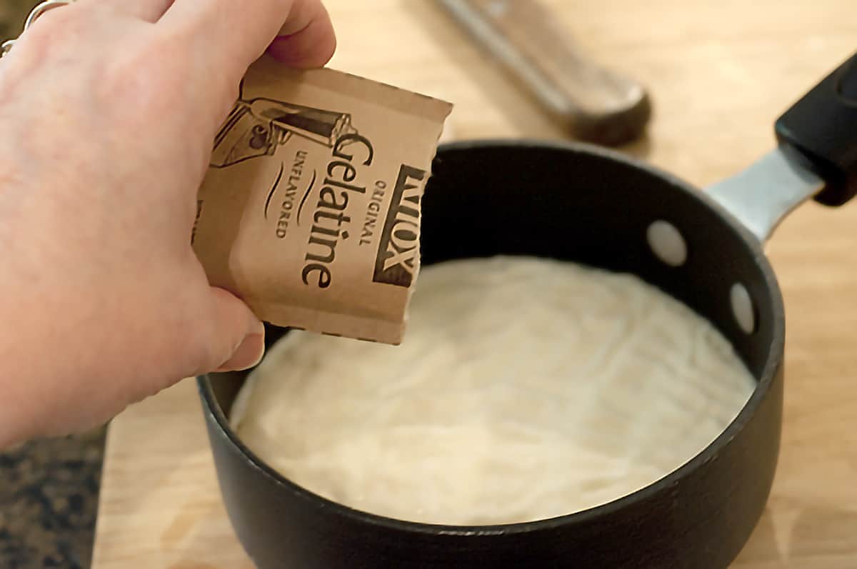 Pouring a packet of gelatin into milk in a small saucepan.