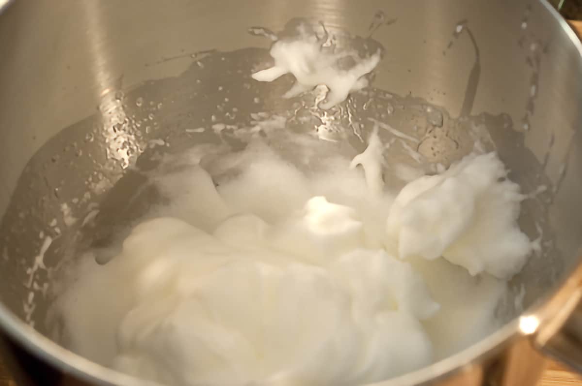 Large mixing bowl containing beaten egg whites.