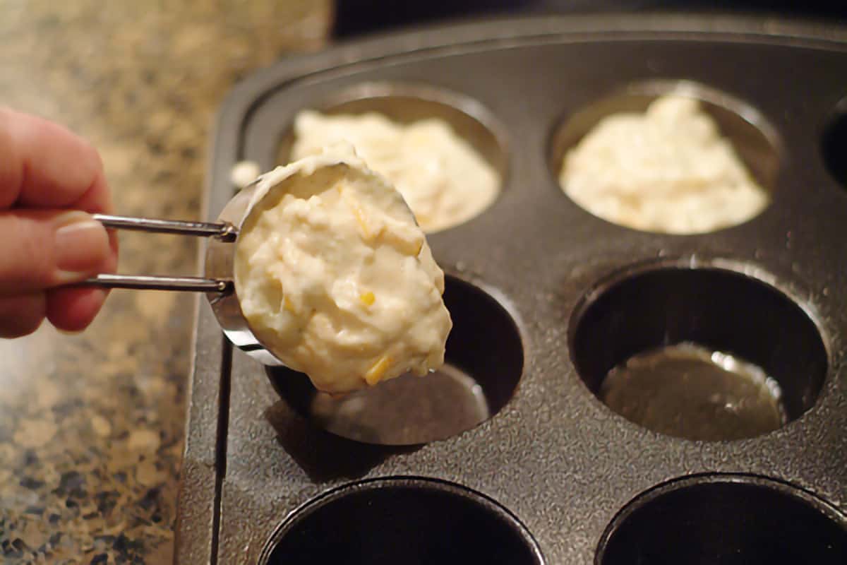 One-fourth cup of batter being placed in each muffin tin cup.
