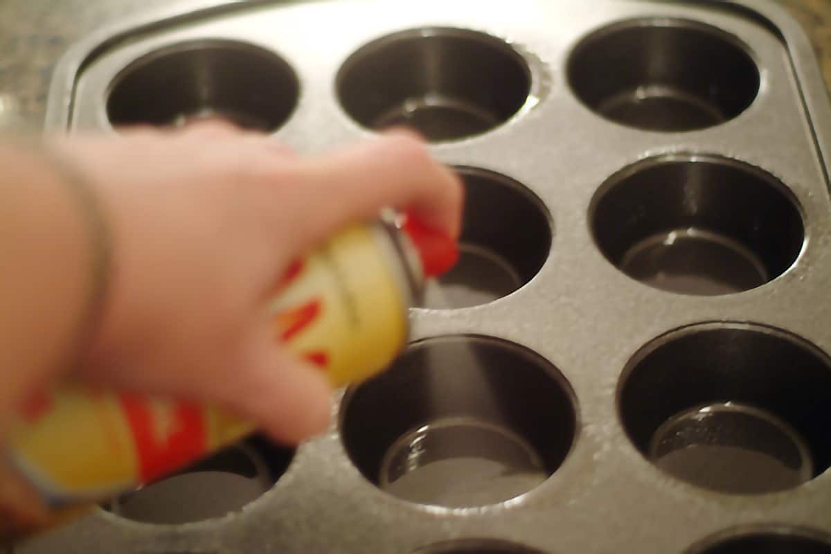 Spraying muffin pan with cooking spray.