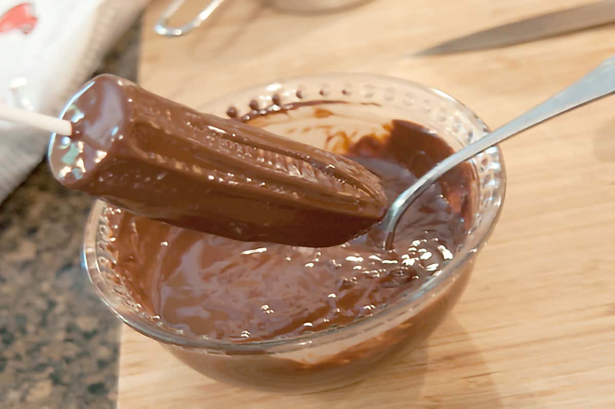 Banana half being coated with melted chocolate.