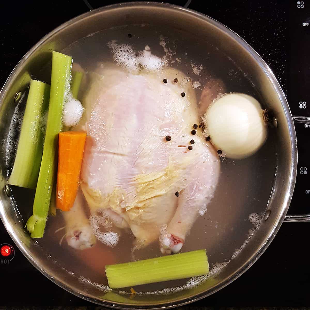 Whole chicken and aromatics simmering in a pot.