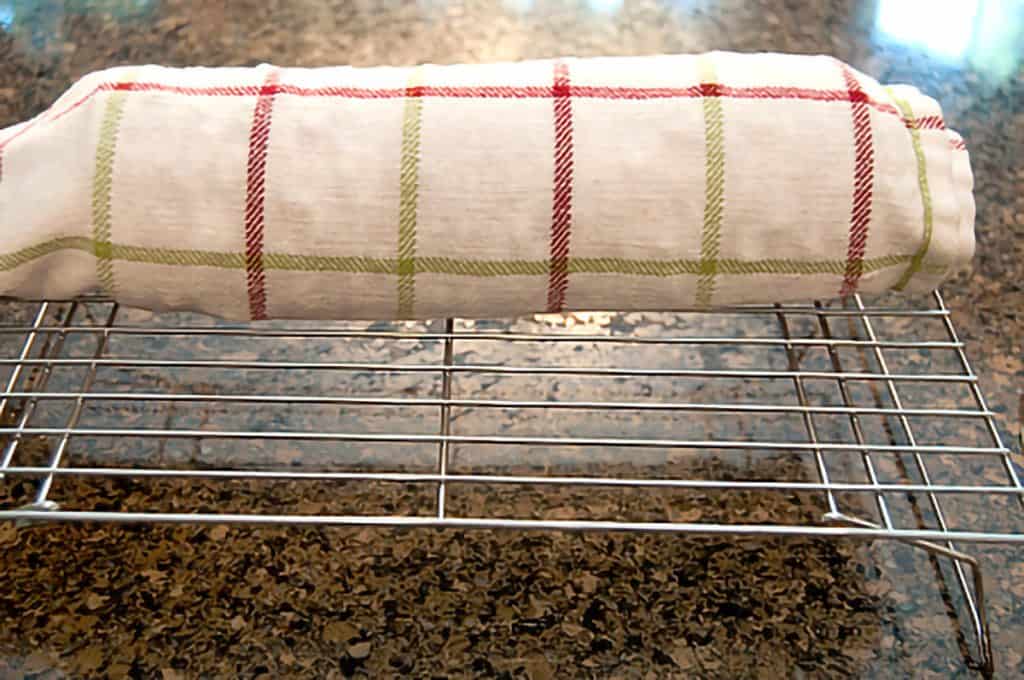 Cake rolled in a tea towel resting on a metal cooling rack.
