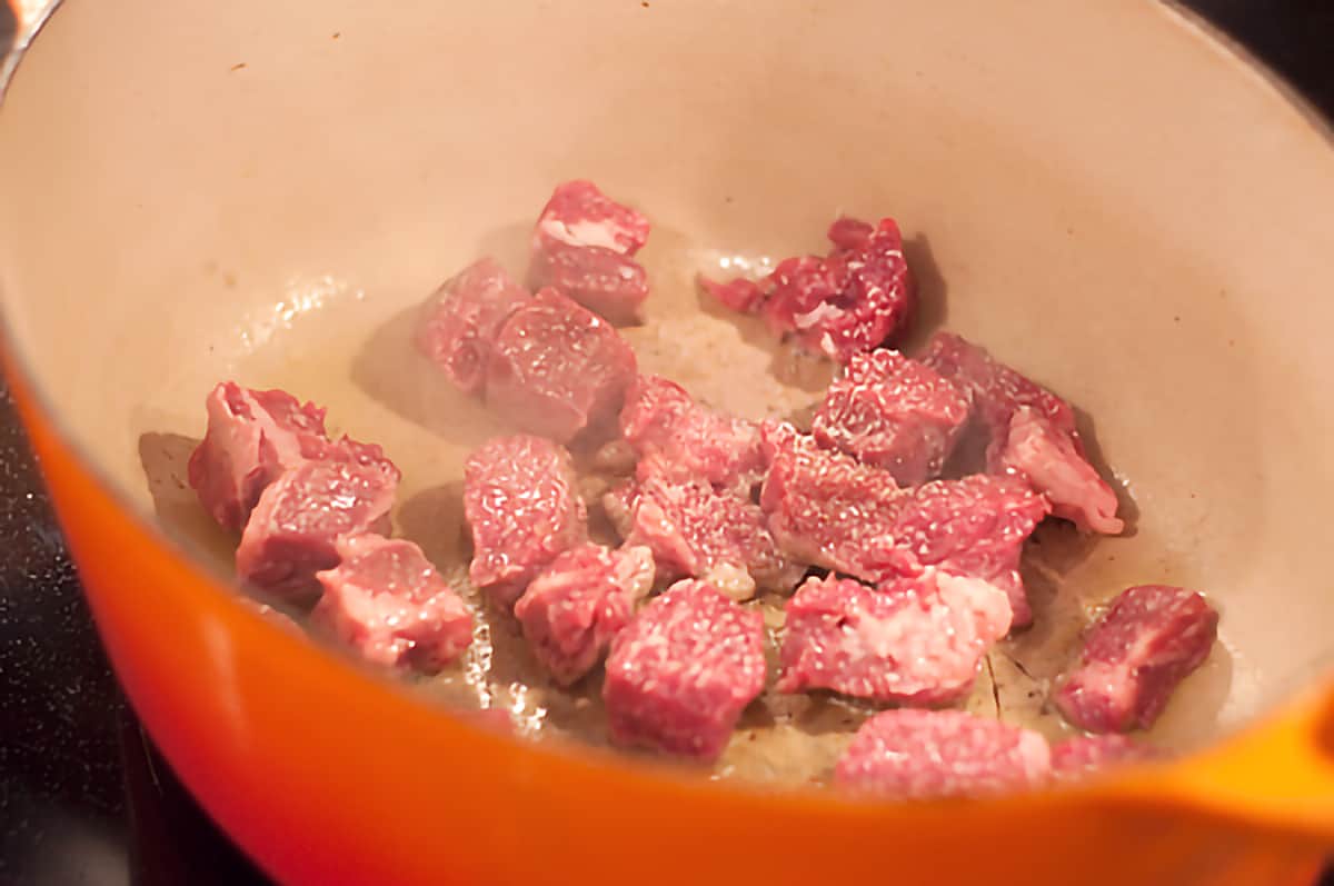 Beef cubes sauteing in a heavy coated cast iron pan.