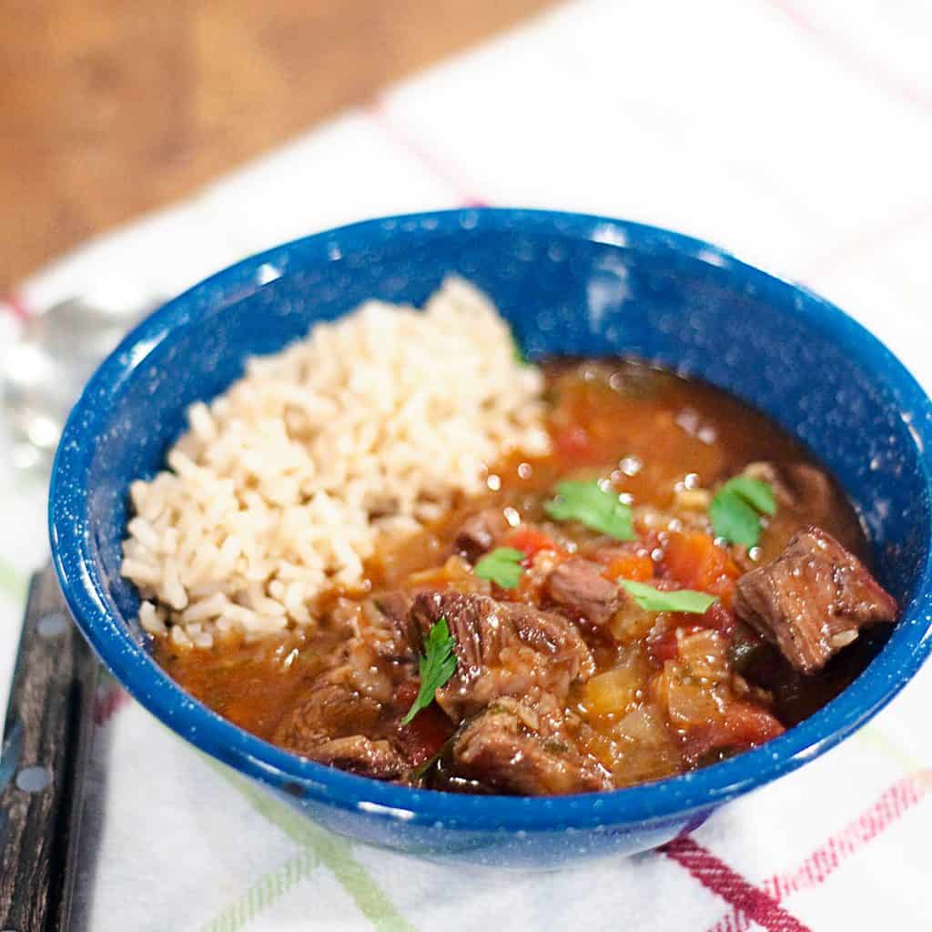 A serving of Garlicky Beef Stew with brown rice in a blue bowl.