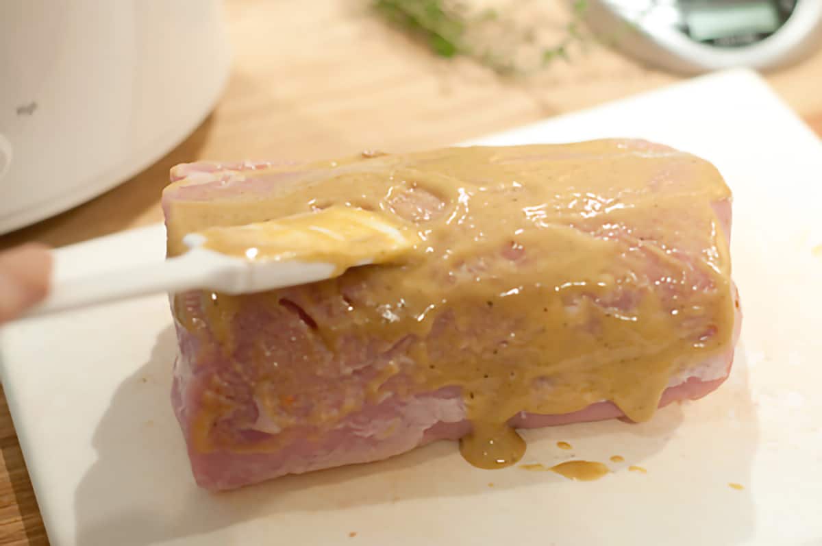 Pork loin on a cutting board coated with mustard misture.