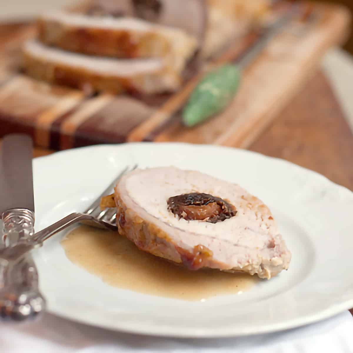 Plated pork loin A slice of the finished Apricot and Prune Stuffed Pork Loin on a white serving plate with antique cutlery.