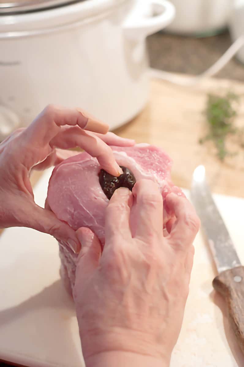 Hands demonstrating how to insert the apricots and prunes into the channel in the pork loin.