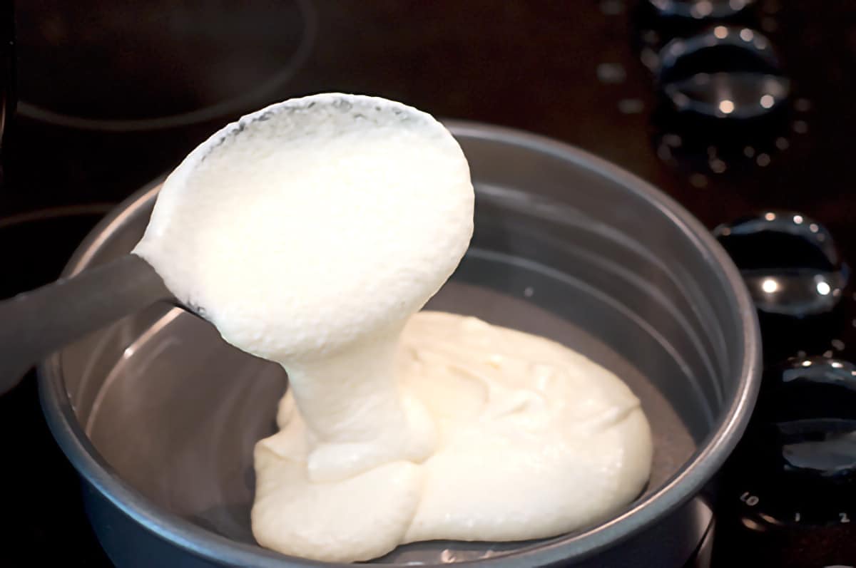 A large cooking spoon full of cake batter being poured into a baking pan.