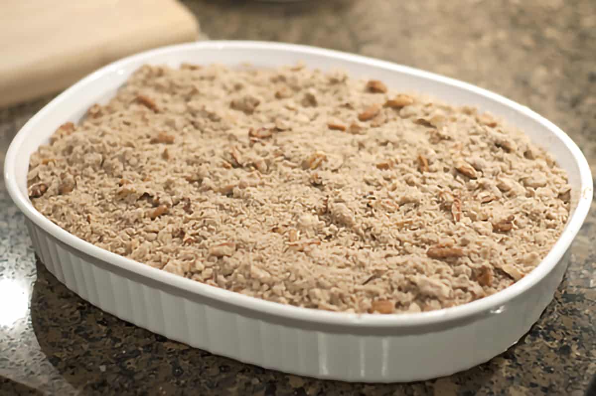 Gingerbread, sugar, and pecan mixture sprinkled over baking dish filled with apple pie filling and gingerbread.