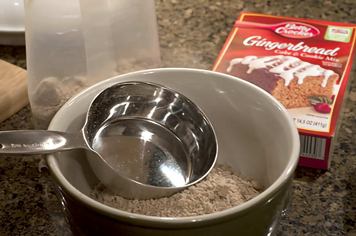Boxed gingerbread mix in a mixing bowl with a measuring cup.