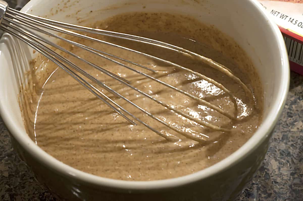 Gingerbread and water mixture in mixing bowl with metal whisk.