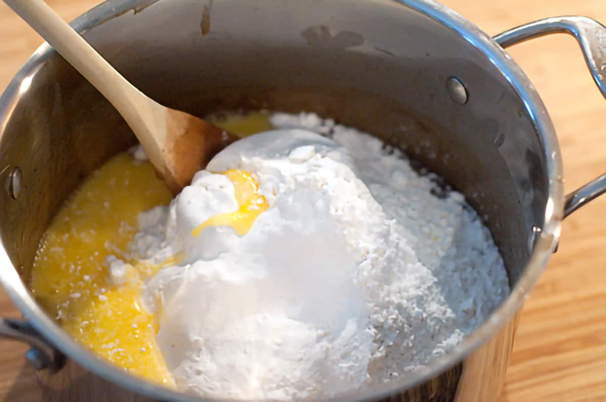 Stirring the flour and eggs into the boiled mixture in the saucepan.