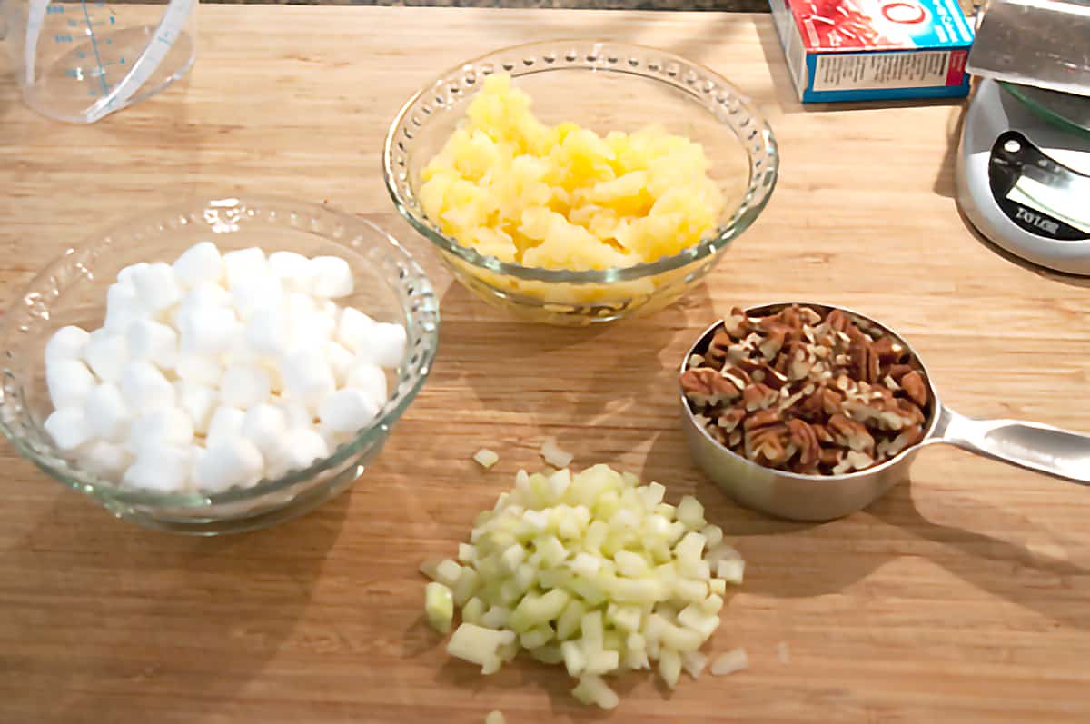 Mini marshmallows, pineapple, chopped pecans, and chopped celery in small bowls.