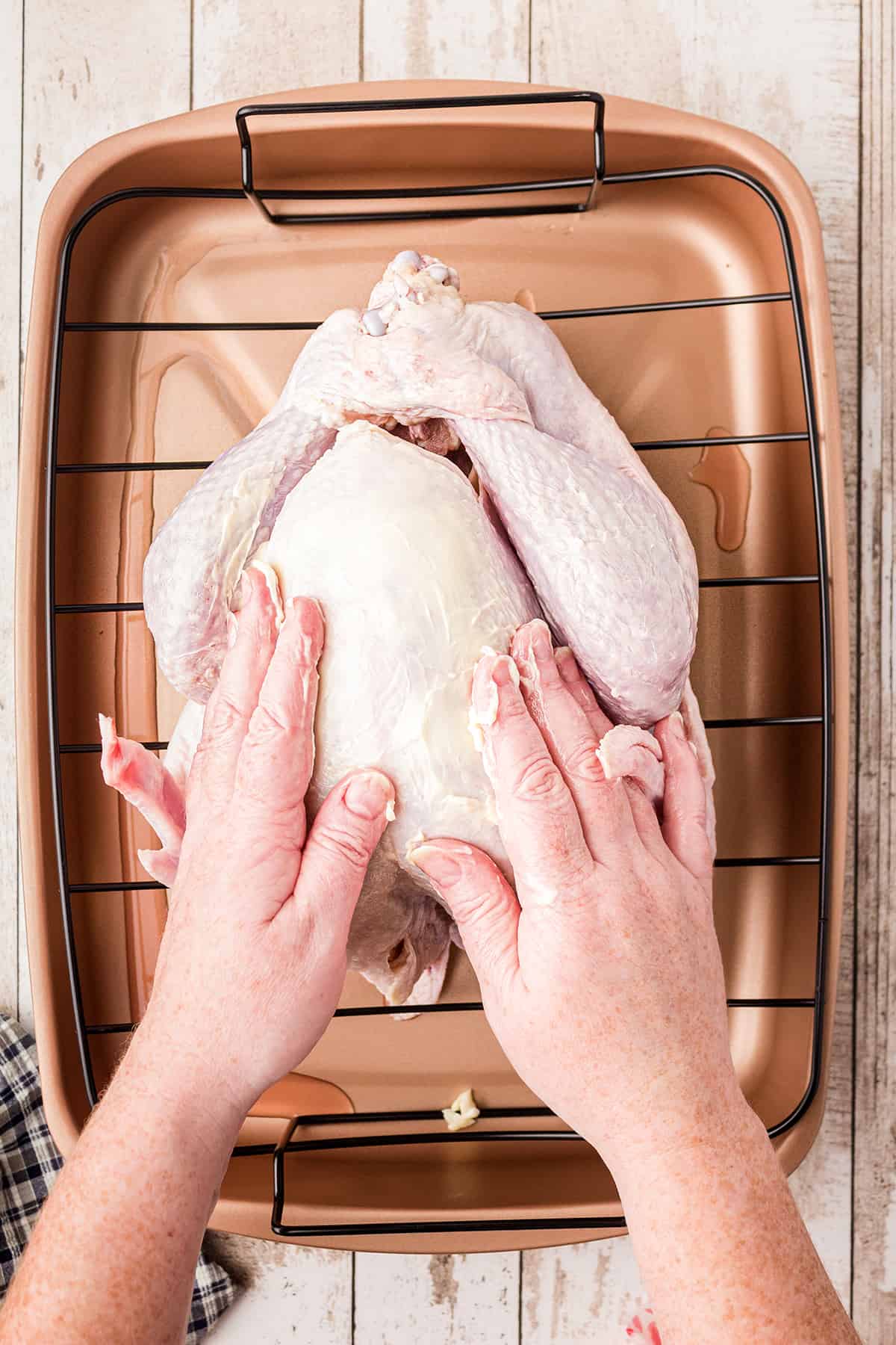 Turkey in a roasting pan being rubbed with butter.
