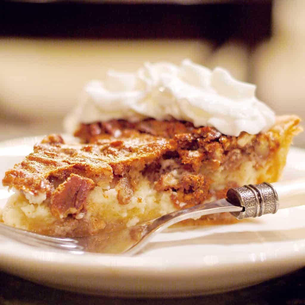 A slice of Pecan Cheesecake Pie on a serving plate with a fork alongside.