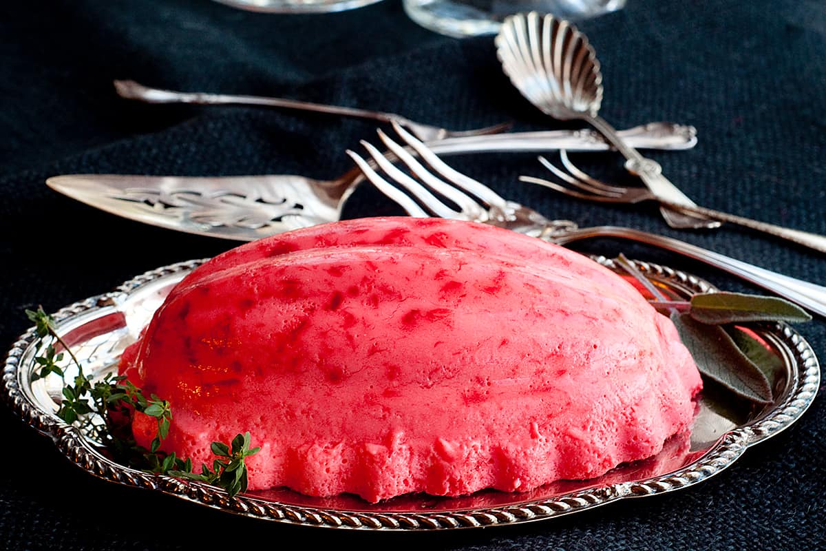 Raspberry Jello Mold on a silver serving tray with vintage serving pieces in the background.