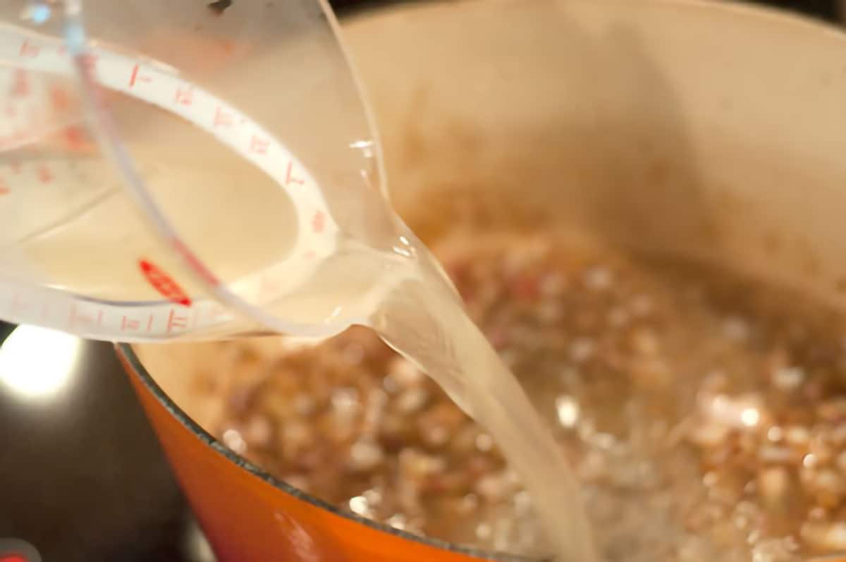 Pouring stock from a measuring cup into the browned shallots in pan.