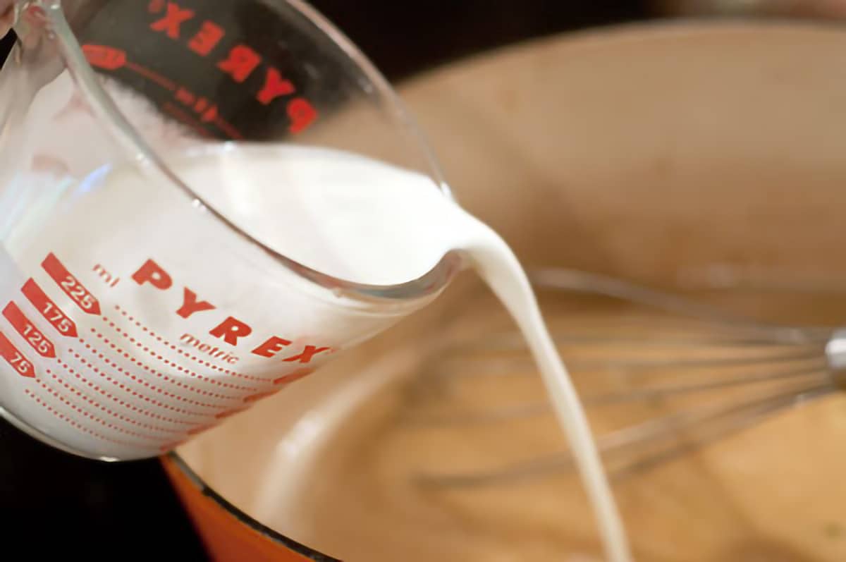 Cream being poured from a measuring cup into the pan sauce.