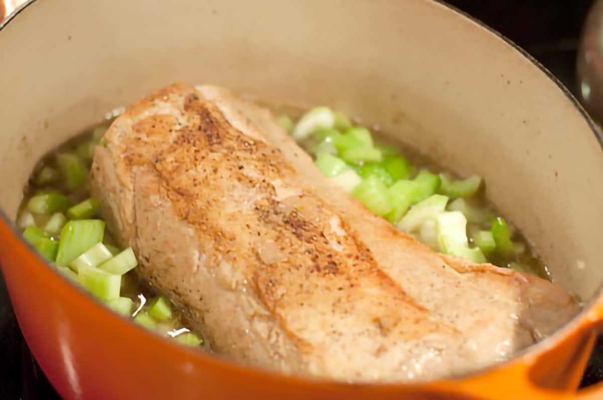 Browned pork loin and celery added into the pan with stock and shallots.