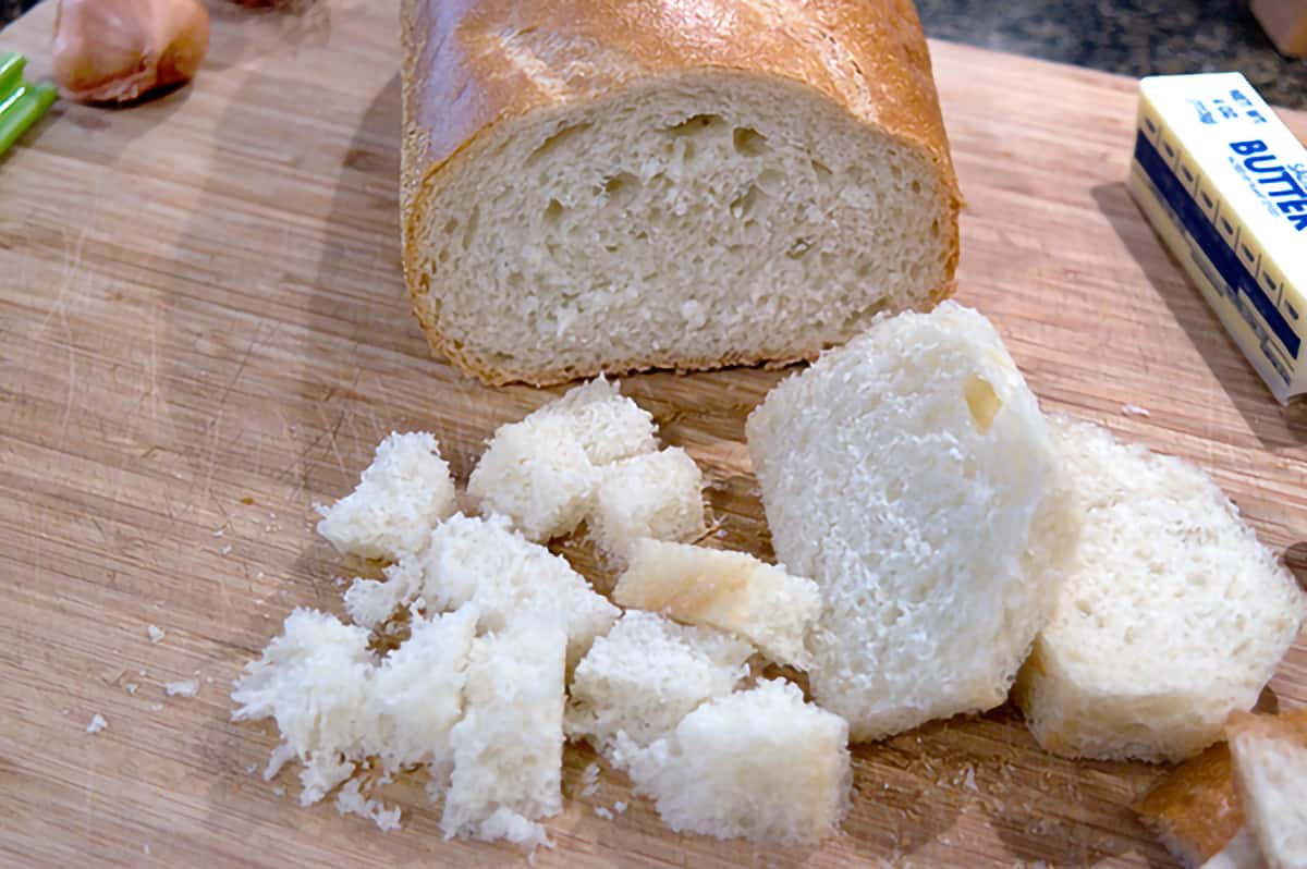 A loaf of Italian bread cut into cubes on a cutting board.