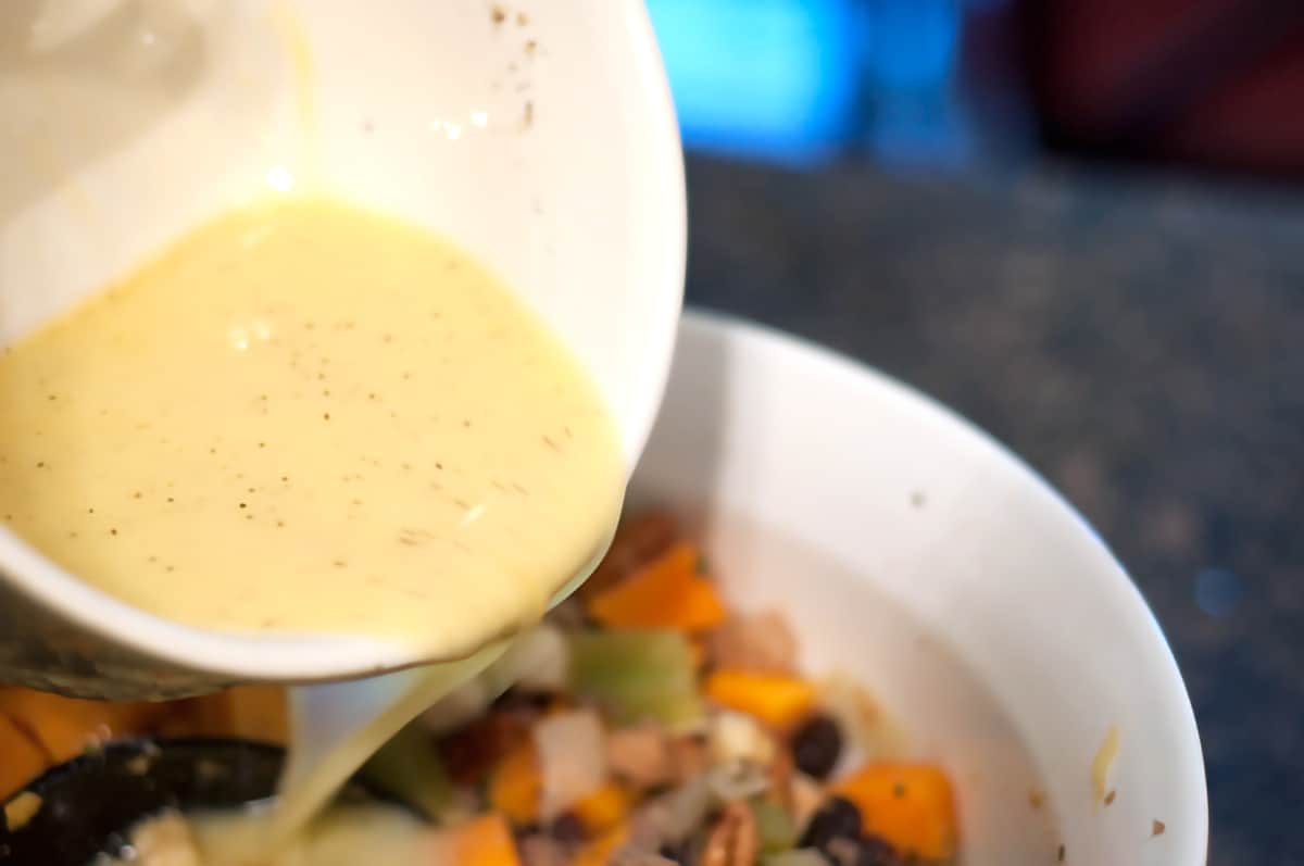 Pouring egg-chicken broth mixture from a small mixing bowl into the stuffing mixture.