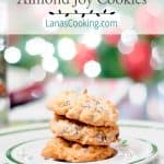Almond Joy Cookies on a Christmas plate with twinkling lights in the background. Text overlay for pinning.
