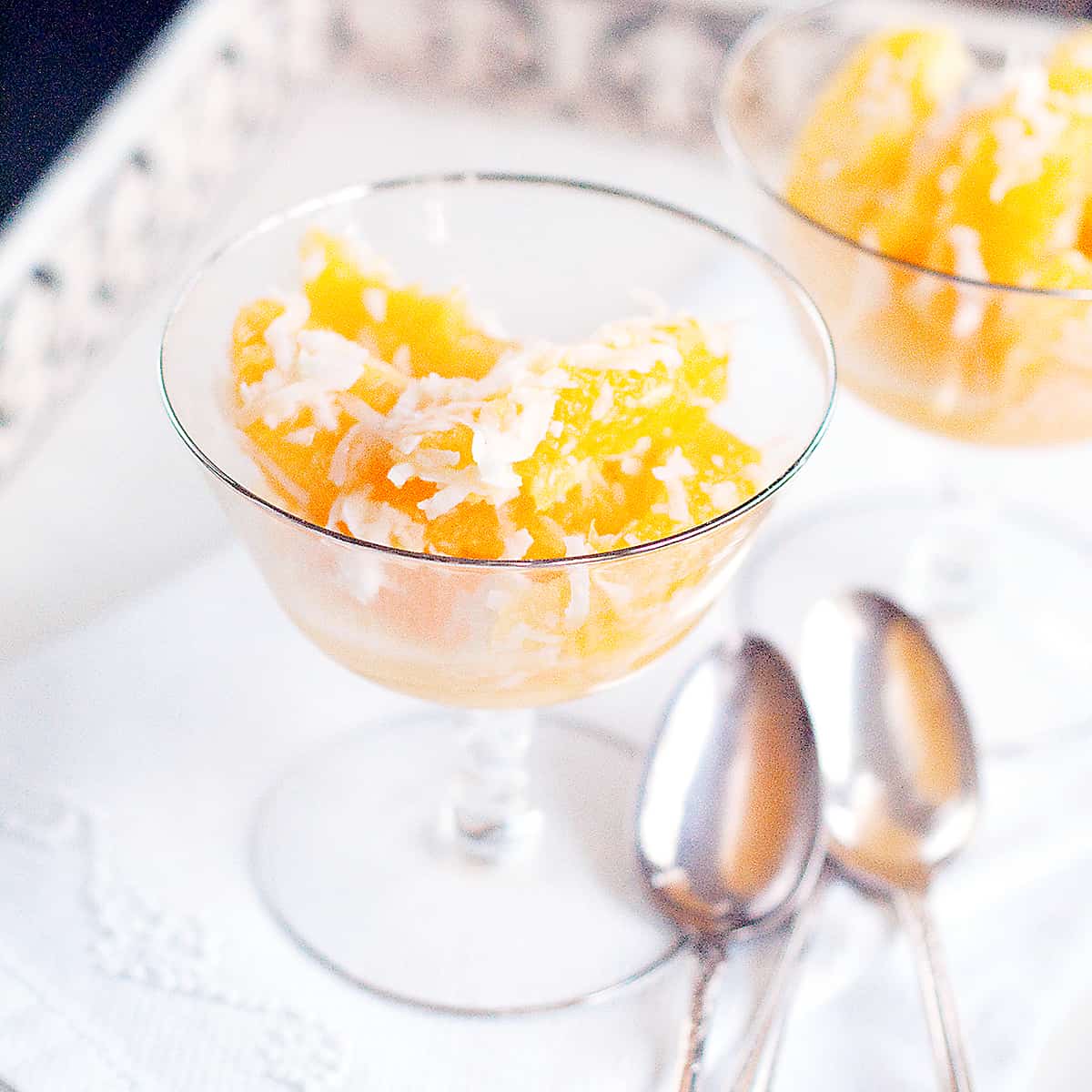 Crystal dish of ambrosia on a serving tray with vintage spoons in the foreground.