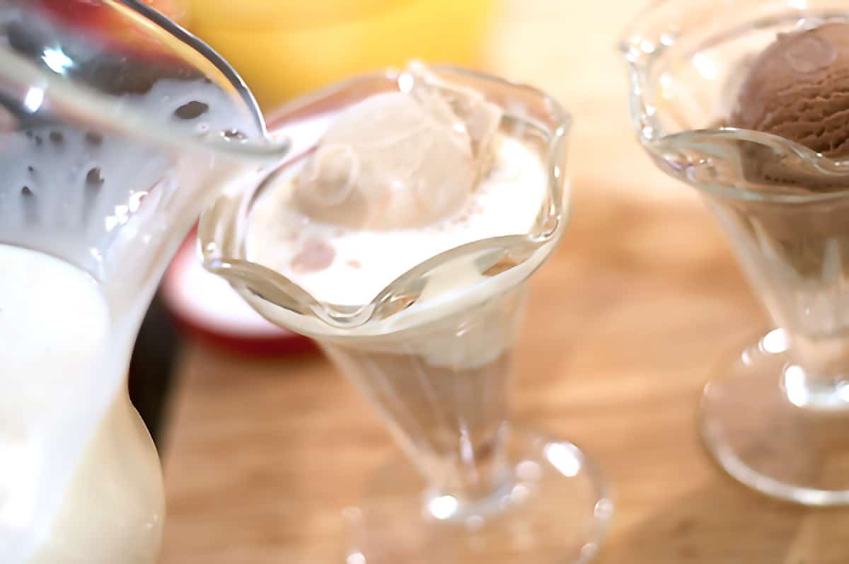 Eggnog being poured from a pitcher over scoops of ice cream