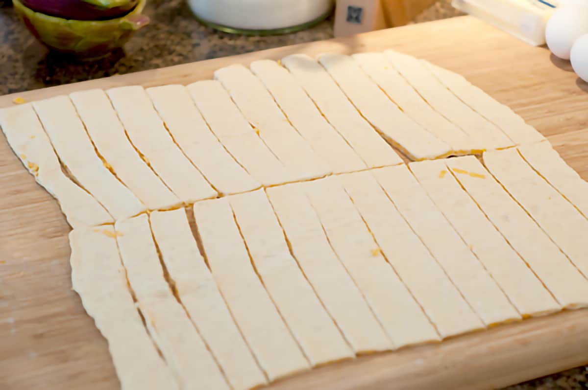 Puff pastry cut into strips on a cutting board.