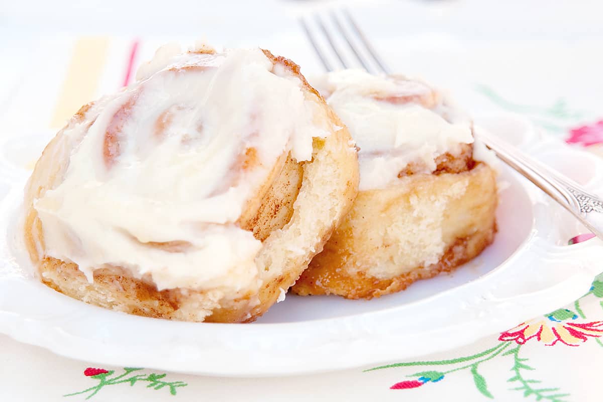 Two cinnamon rolls with cream cheese icing on a white plate with a fork on the side.