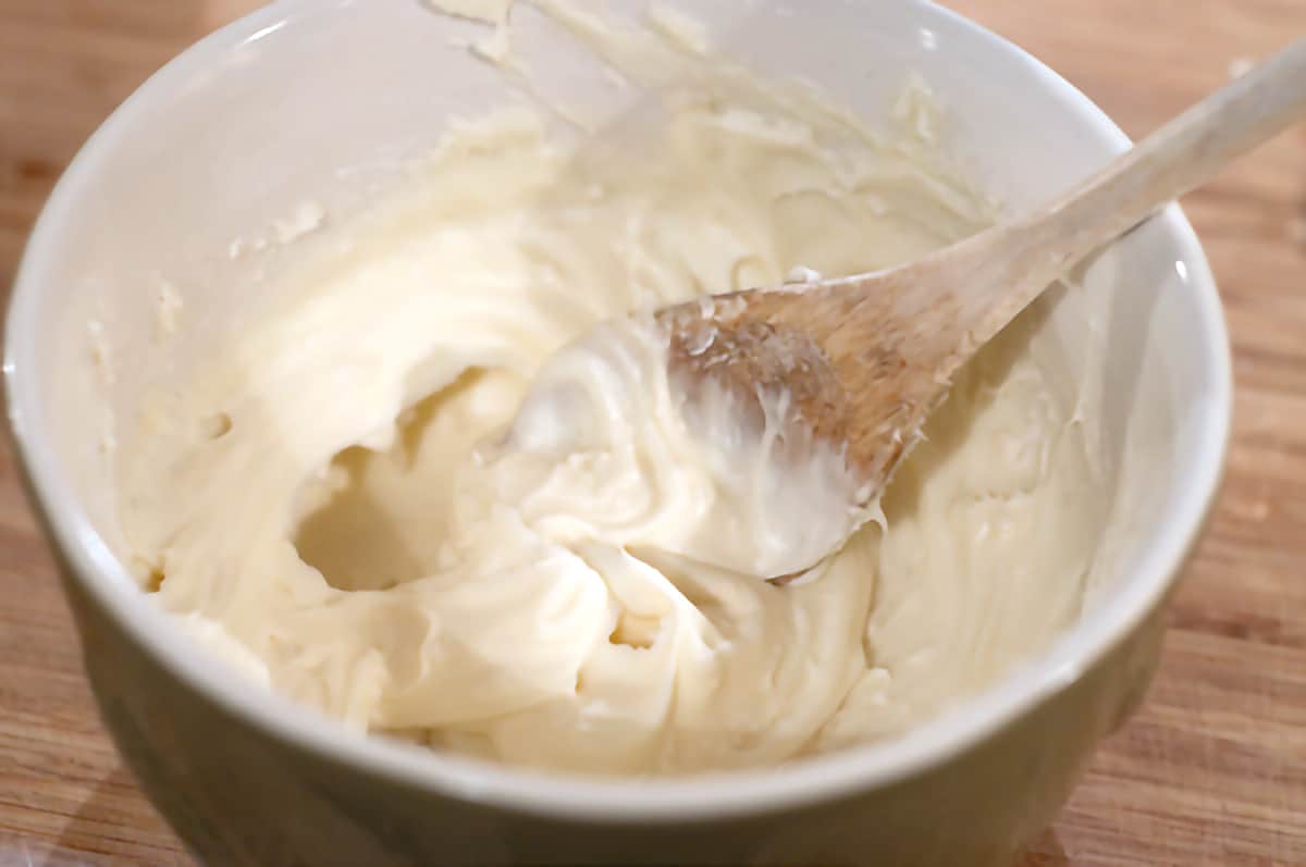 Mixing bowl with cream cheese icing and a wooden spoon.