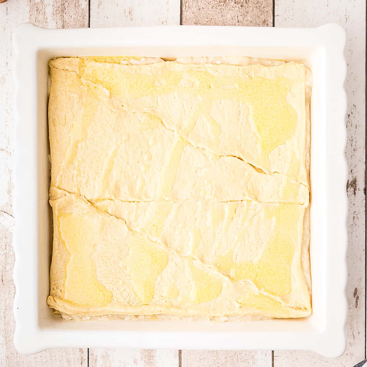 Prepared and filled crescent roll dough in pan topped with melted butter.