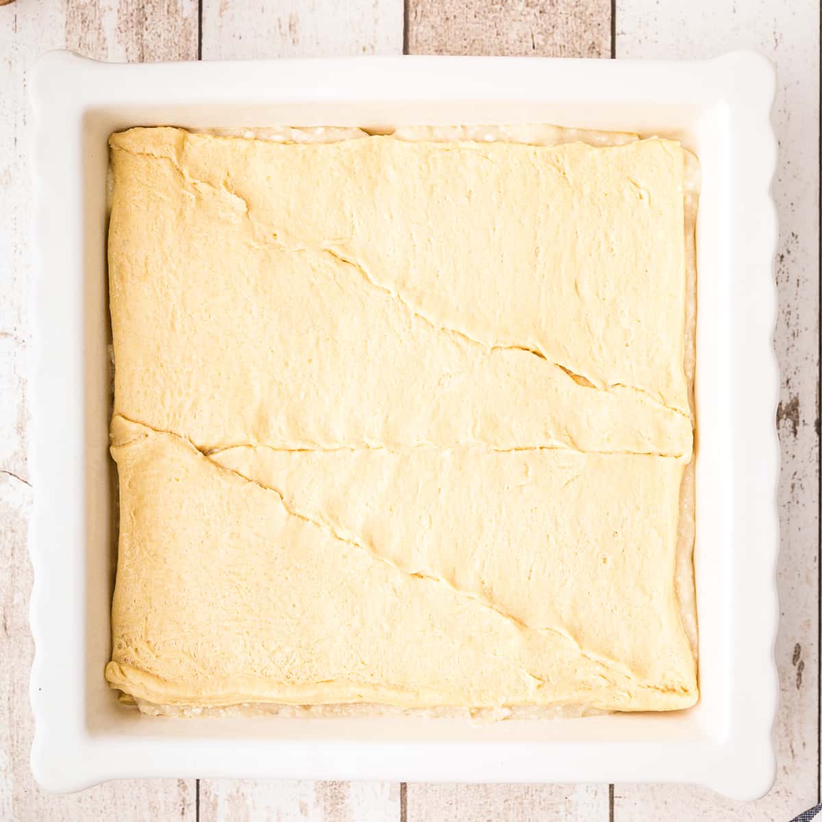 Baking pan with crescent roll dough filled with cream cheese mixture and topped with second sheet of crescent roll dough